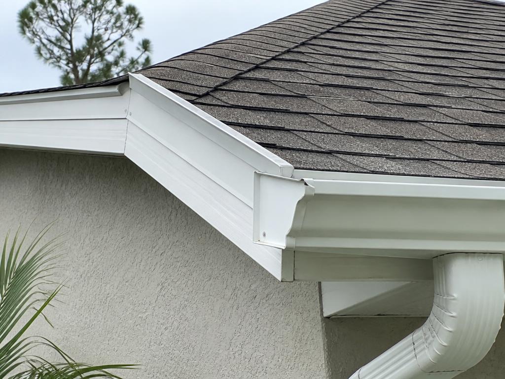 Edge of a shingle roof in Bradenton, Florida, showing drip edge, underlayment, and gutter apron sequenced to shed water into the gutter.